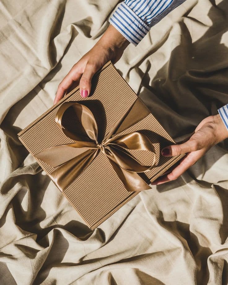 Hands holding a kraft-paper gift tied with a gold ribbon